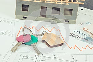 Keys, euro and downward graphs representing crisis of real estate market. Reduced housing prices. House under construction