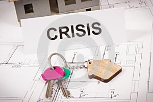 Keys with house shape and inscription crisis on housing plan. Crisis of real estate market. Reduced housing prices