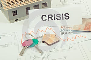 Keys, inscription crisis, euro and downward graphs representing crisis of real estate market. Reduced housing prices. House under