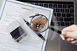 Keys with wooden house, magnifying glass and contract on a laptop. Concept of rent, search or mortgage
