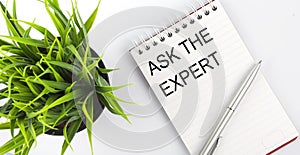 Keyword ASK THE EXPERT - business concept text on a white notebook and pen, green flowers