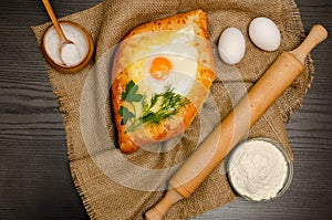 Khachapuri with eggs on sackcloth, flour, eggs and salt on black table