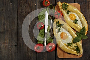 Khachapuri with fresh vegetables caucasian kitchen, close-up on a black wooden table. Adzharian khachapuri. View from above