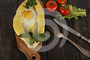 Khachapuri with fresh vegetables caucasian kitchen, close-up on a black wooden table. Adzharian khachapuri. View from above