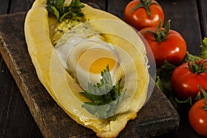 Khachapuri with fresh vegetables caucasian kitchen, close-up on a black wooden table. Adzharian khachapuri. View from above