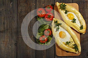 Khachapuri with fresh vegetables caucasian kitchen, close-up on a black wooden table. Adzharian khachapuri. View from above