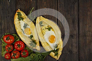 Khachapuri with fresh vegetables caucasian kitchen, close-up on a black wooden table. Adzharian khachapuri. View from above