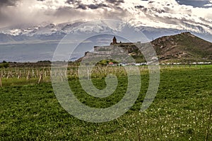 Khor Virap fortress on a rocky hill in the Ararat valley against the background of clouds descending on mount Ararat