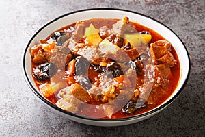 Khoresht Aloo Stewed lamb meat with dried plums or prunes, tomato, onion, potato, carrot and garlic closeup in the bowl.