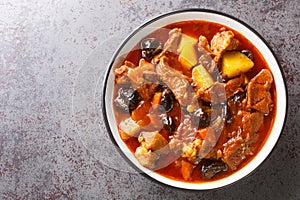 Khoresht Aloo Stewed lamb meat with dried plums or prunes, tomato, onion, potato, carrot and garlic closeup in the bowl.