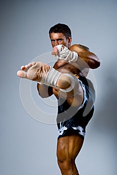 Kick-boxer kicks on a gray background.