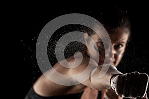 Kickboxer girl with magnesium powder on her hands, punching with dust visible