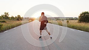 The kickboxer with hood on head training kicks on country road during sunset