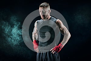 Kickboxer in red bandages stands against a background of smoke. The concept of mixed martial arts