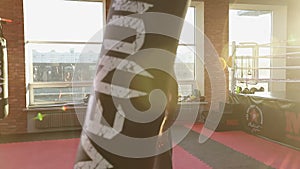 Kickboxing black man training punching bag in fitness studio with large windows.
