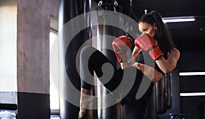 Kickboxing woman in activewear and red kickboxing gloves on black background performing a martial arts kick