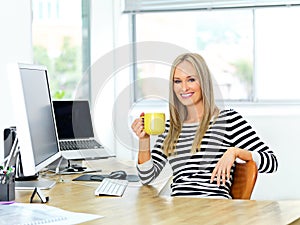 Kickstart your day with some java. Shot of a beautiful young woman working at her office desk while enjoying a drink.