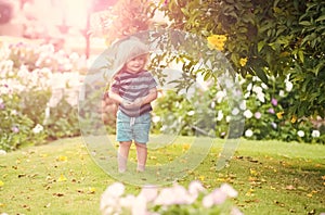 Kid baby outdoor in garden with flowers and green grass on natural background, summer kids vacation, childhood and