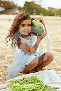 Kid On Beach Portrait. Cute Little Girl With Curly Hair Holding Watermelon. Happy Child Going To Eat On Sandy Coast.