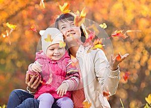 Kid and beautiful mother play and throw leaves outdoor in autumn