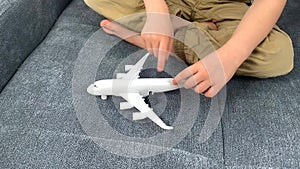 Kid in black glasses plays with a white airplane toy, concept of flight, travel