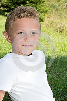 Kid blond boy child in white t-shirt in green grass field park home garden