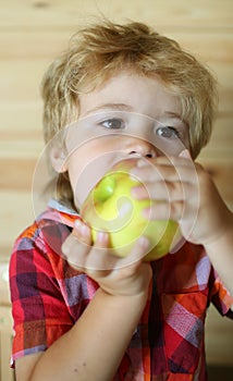 Kid or blonde happy boy eating apple.