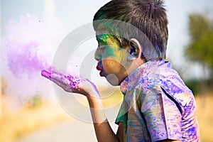 Kid blowing holi colour powder from hand during Holi festival celebration - Concept of young kids having fun by playing holi