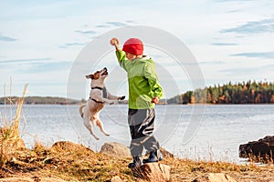 Kid boy balancing on stone playing with dog jumping high for toy. Family rests on beach on Autumn day