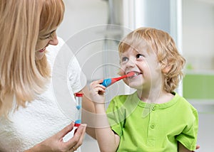 Kid boy brushing teeth in bathroom. His mother monitoring accuracy and time of cleaning action with hourglass.