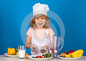 Kid boy in chef hat and apron cooking blueberries smoothie . Little cook with vegetables at kitchen. Natural kids food.