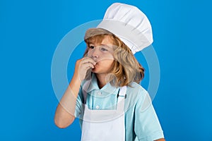 Kid boy in chef hat and apron cooking preparing meal. Little cook with vegetables at kitchen. Natural kids food.