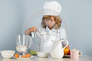 Kid boy in chef hat and apron cooking preparing meal. Little cook with vegetables at kitchen. Natural kids food.