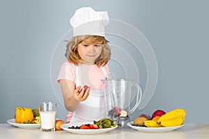 Kid boy in chef hat and apron cooking preparing meal. Little cook with vegetables at kitchen. Natural kids food.