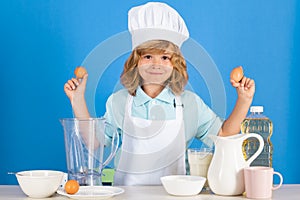 Kid boy in chef hat and apron hold eggs cooking preparing meal. Little cook with vegetables at kitchen. Natural kids