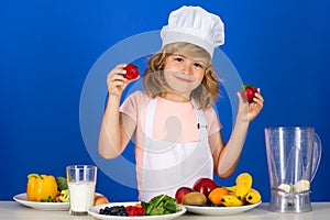 Kid boy in chef hat and apron hold strawberries cooking preparing meal. Little cook with vegetables at kitchen. Natural