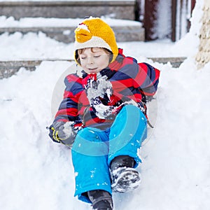 Kid boy in colorful clothes having fun with riding on snow, outd