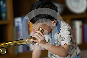Kid or boy concentrates telescope indoors