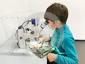 Kid boy conducts experiment with microscope in school lab. Curious inquisitive child learning physics and computer