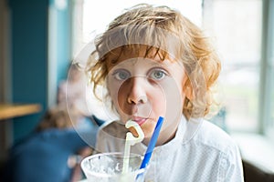 Kid boy with curly hair drinking milkshake and looking at camera