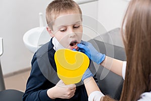 Kid boy in dentist`s chair looks in the mirror and the doctor in blue gloves shows him his teeth