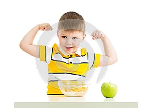 Kid boy eating healthy food and showing his strength