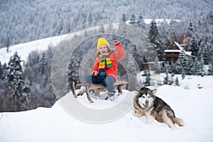 Kid boy enjoy a sleigh ride. Kid sledding in winter snow outdoor. Christmas family vacation. Child boy ride on a wooden