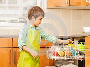 Kid boy getting out clean crockery of dishwasher