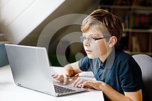 Kid boy with glasses learning at home on laptop for school. Adorable child making homework and using notebook and modern