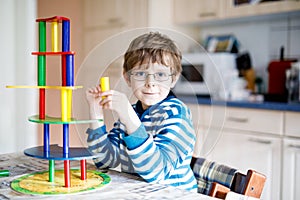 Kid boy with glasses playing with lots of colorful wooden blocks game indoor