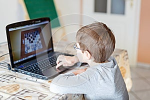 Kid boy with glasses playing online chess board game on computer