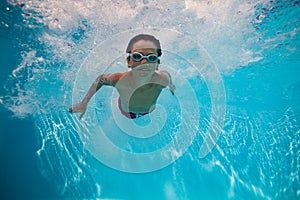 Kid boy with goggles swimming underwater joyfully after dive