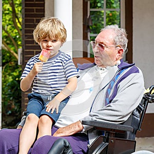 Kid boy and grandfather on wheelchair eating ice cream