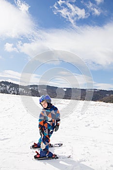 Kid boy in helmet, winter overalls skiing in the snowy mountains